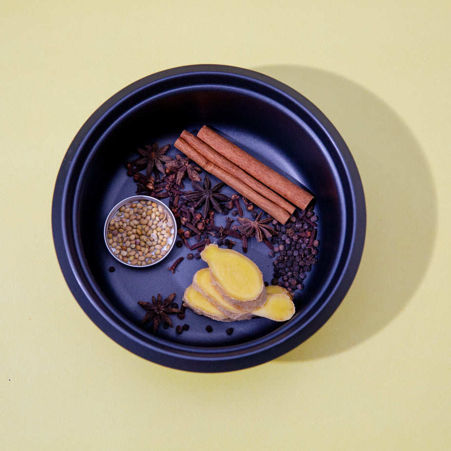 Traditional Chinese ingredients including star anise, ginger, and spices arranged in blue ceramic bowl on beige background
