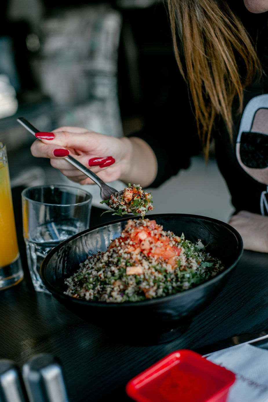Person eating colorful grain bowl filled with roasted vegetables, greens, and grains in black bowl