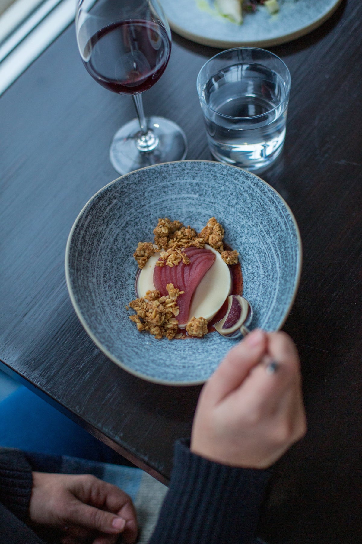 Bowl of yogurt with strawberries and granola held over blue surface